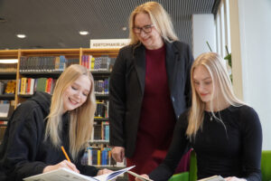 Opettaja ja kaksi opiskelijaa iloisesti pöydän ääressä