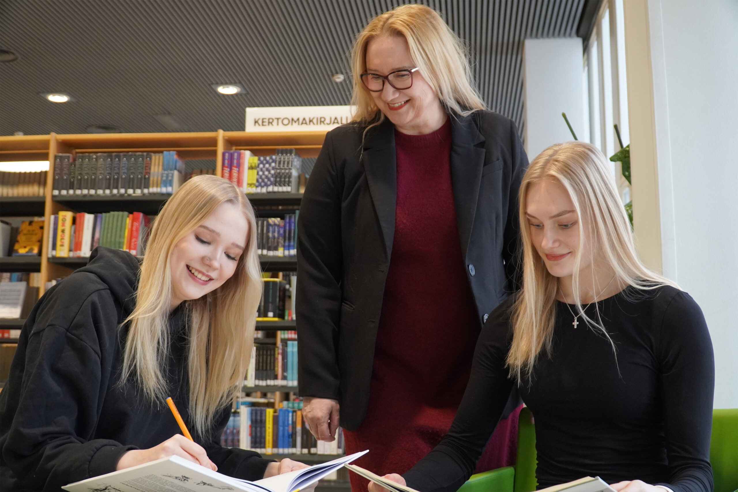 Opettaja ja kaksi opiskelijaa iloisesti pöydän ääressä
